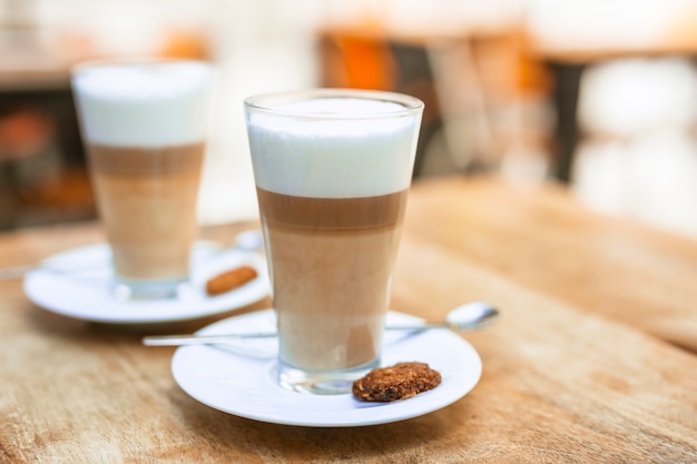 Deux verres à café cappuccino avec une cuillère et une soucoupe sur une table en bois