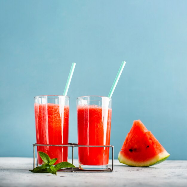 Deux verres avec du jus de melon d'eau et une tranche à côté