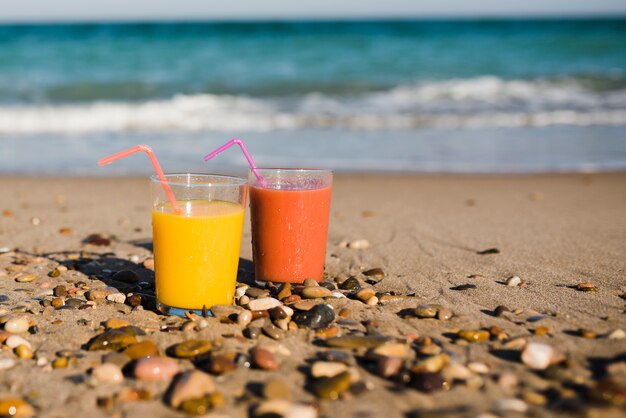 Deux verres de jus avec de la paille sur une plage de sable près du bord de mer