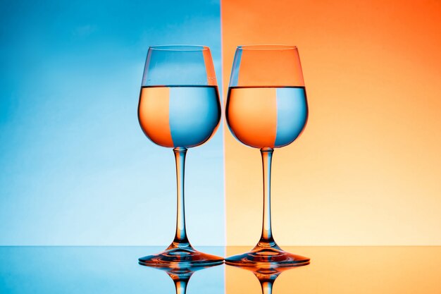 Deux verres à vin avec de l'eau sur fond bleu et orange.