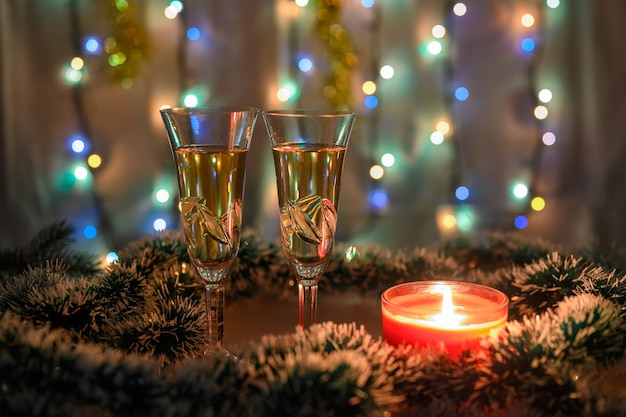 Deux verres de vin mousseux entourés de guirlandes vertes et blanches avec une bougie allumée et une guirlande lumineuse sur fond de nouvel an.