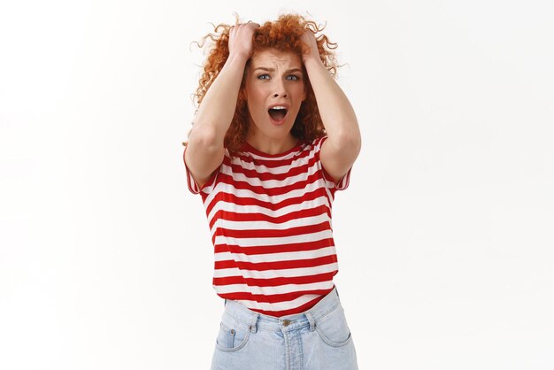 Dévasté concerné paniquer jeune rousse sous pression femme aux cheveux bouclés criant regard déprimé frustré en détresse tirer les cheveux de la tête troublé debout dérangé pissé fond blanc