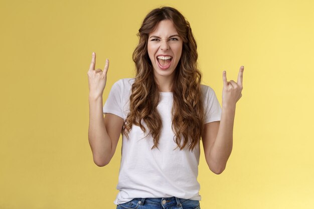 Devenir sauvage. Audacieuse amusée belle fille européenne aux cheveux bouclés agissant ravie excitée s'amuser profiter d'un spectacle de concert génial ouais geste de heavy metal rock-n-roll grimaçant satisfait