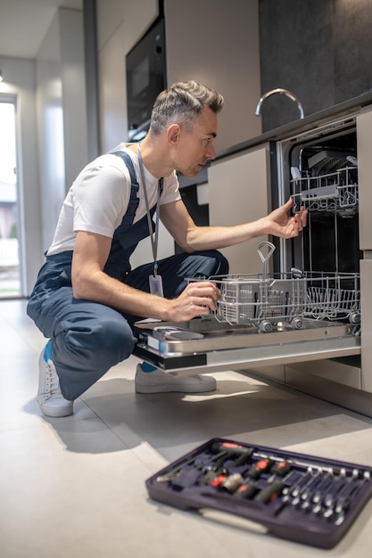 Diagnostic de l'équipement Profil d'un homme sérieux regardant un lave-vaisselle ouvert dans la cuisine