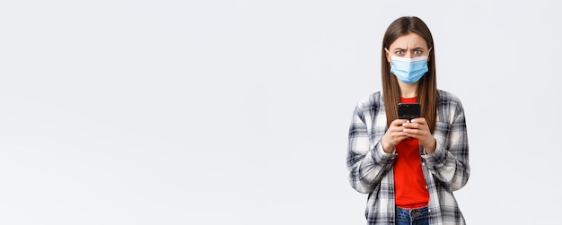 Photo gratuite différentes émotions covid19 distanciation sociale et concept technologique une jeune femme frustrée et confuse portant un masque médical réagit à un message étrange tenir un téléphone portable en fronçant les sourcils