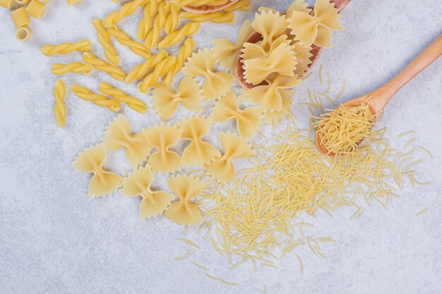 Différentes formes de pâtes et cuillères crues sur un espace blanc.