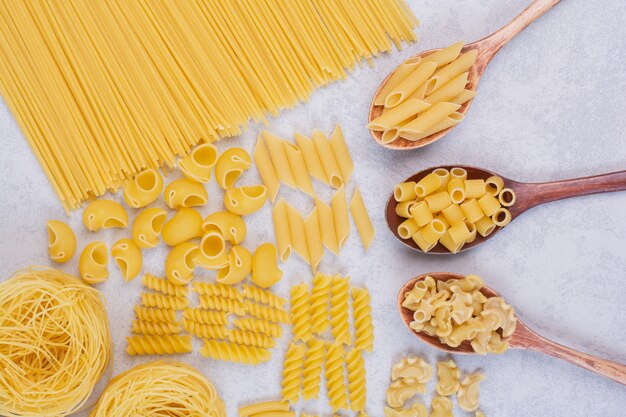 Différentes formes de pâtes et cuillères crues sur une surface blanche