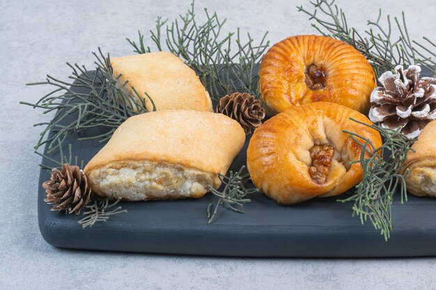 Différents cookies, pomme de pin et branche de pin sur un plateau en bois, sur le marbre.