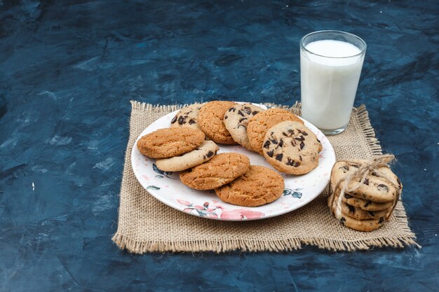 Différents types de biscuits, du lait sur un napperon sur un fond bleu foncé. vue grand angle.