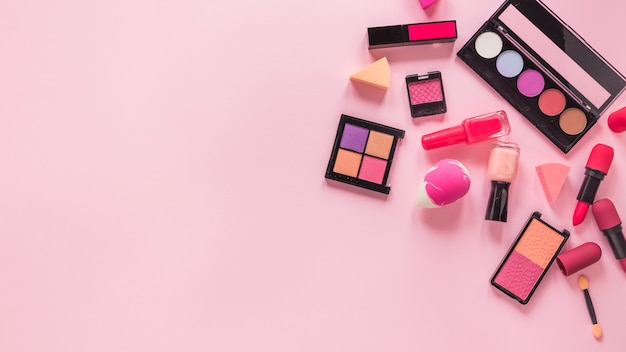 Différents types de cosmétiques dispersés sur une table rose
