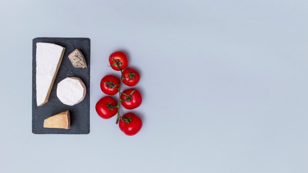 Différents types de fromages sur une ardoise noire avec des tomates rouges sur une surface grise avec espace de copie