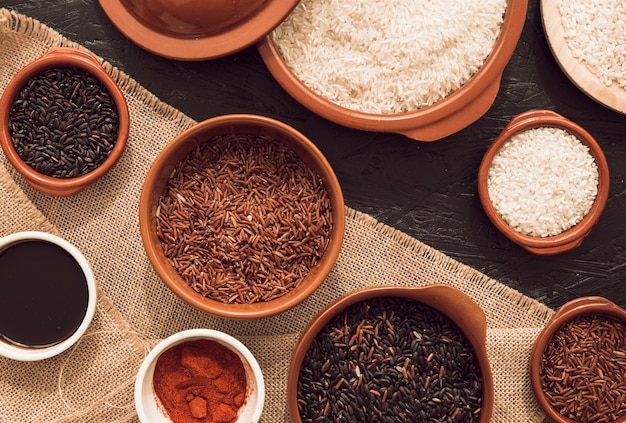 Différents types de grains de riz biologiques sur le sac et fond de texture rugueuse