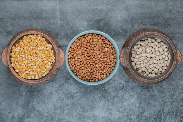 Différents types de haricots et de maïs non cuits dans divers pots.