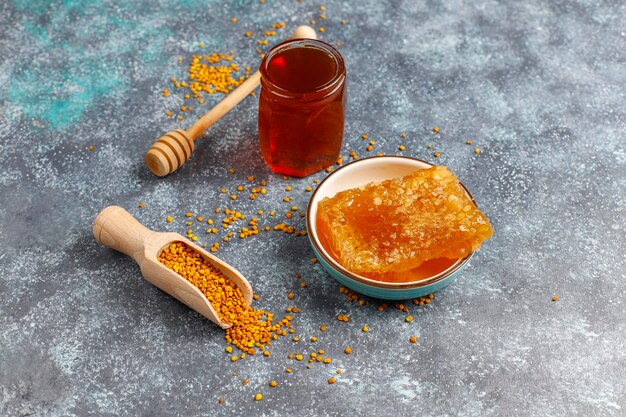 Différents types de miel dans des bocaux en verre, nid d'abeille et pollen.