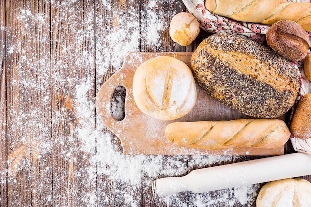 Différents types de pains cuits au four avec de la farine sur la table en bois