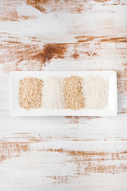 Différents types de riz non cuit dans un petit plateau blanc sur un fond rustique