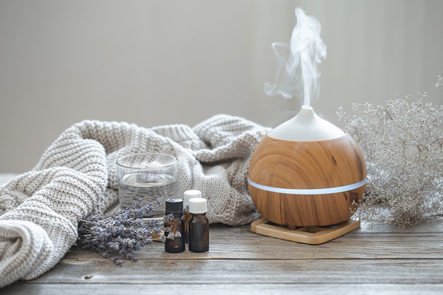 Diffuseur d'huile d'arôme moderne sur surface en bois avec élément tricoté, eau et huiles en pots.