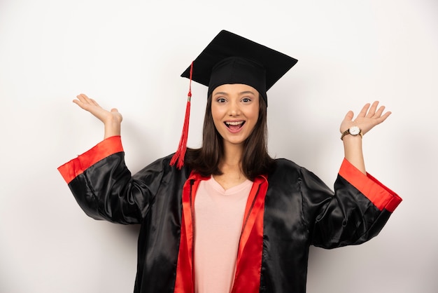 Diplômé frais en robe montrant ses mains sur fond blanc.