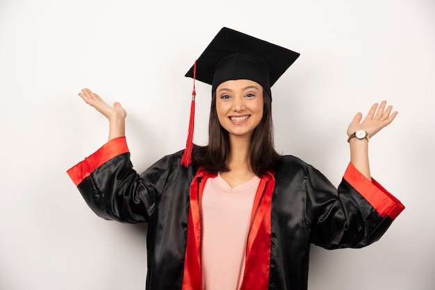 Diplômé frais en robe montrant ses mains sur fond blanc.