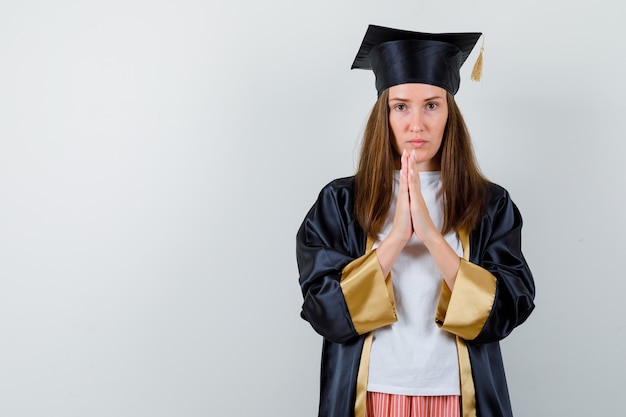 Diplômée féminine gardant les mains en signe de prière en uniforme, vêtements décontractés et à la recherche d'espoir. vue de face.