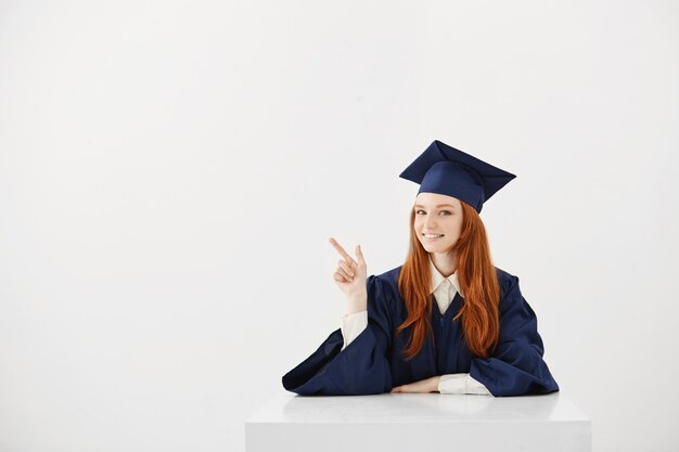 Diplômée de sexe féminin souriant pointant le doigt en position assise.