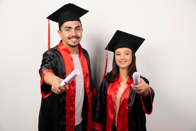 Diplômés frais en robe posant avec diplôme sur blanc.