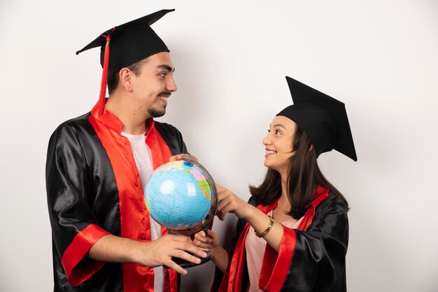 Diplômés frais en robe regardant globe sur blanc.