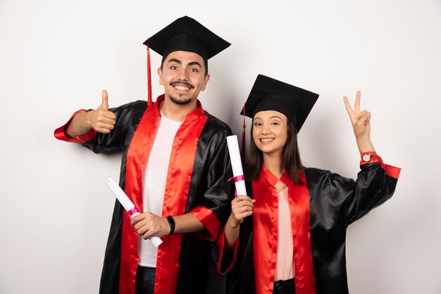 Diplômés frais en robe se sentant heureux avec leur diplôme sur blanc.