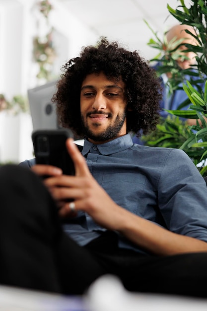 Photo gratuite un directeur exécutif souriant en train d'envoyer des messages sur un réseau social sur son smartphone