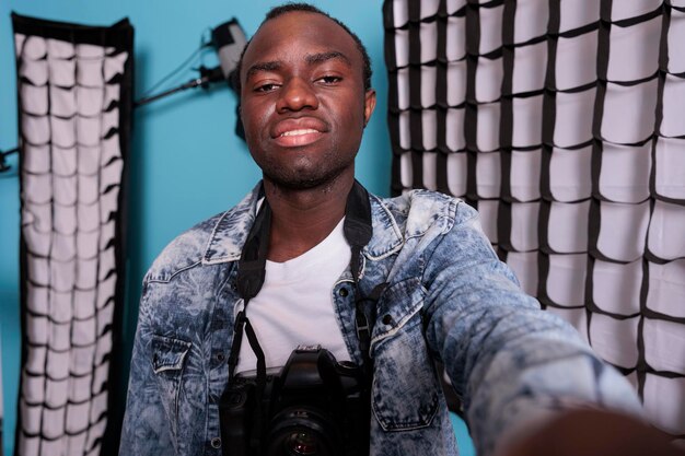 Directeur de studio de production confiant prenant une photo de selfie tout en se tenant à côté d'un équipement de prise de vue professionnel. Passionné de photographie se prenant en photo à côté de softboxes et de projecteurs.