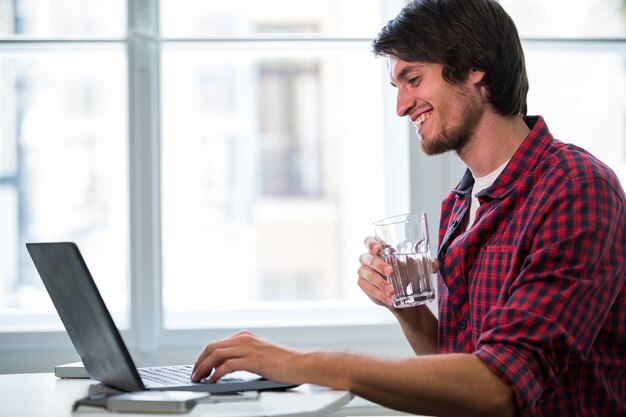 dirigeant d&#39;entreprise Homme ayant un verre d&#39;eau tout en utilisant un ordinateur portable