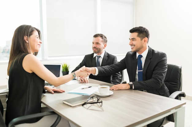 Une dirigeante confiante accueillant des employés masculins avec une poignée de main au bureau