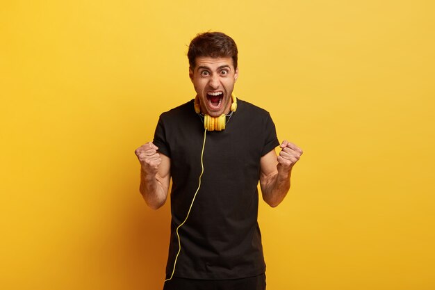 Dites oui à un son exceptionnel. Fou de joie émotionnelle jeune homme caucasien serre les poings, crie fort, porte un t-shirt noir