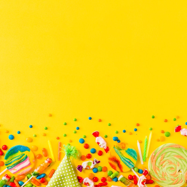 Photo gratuite divers bonbons et chapeau de fête au bas du fond jaune