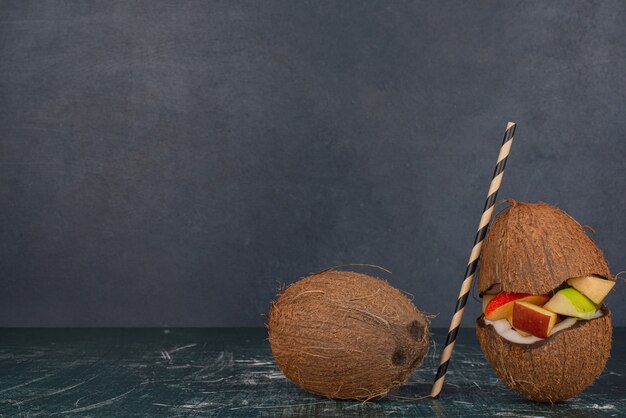 Divers fruits en moitié de noix de coco coupée avec de la paille sur table en marbre