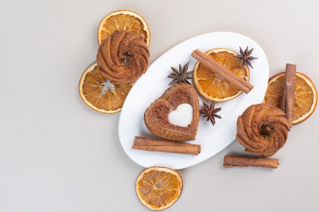 Divers gâteaux avec tranches d'orange, clous de girofle et cannelle sur plaque blanche