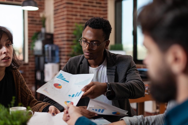 Divers groupes partageant des documents avec des statistiques financières travaillant dans la planification du chiffre d'affaires de l'entreprise, la collaboration commerciale. Hommes d'affaires multiethniques travaillant sur des idées de brainstorming de projet dans un bureau de démarrage