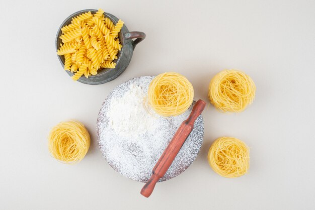 Divers macaronis crus et farine avec rouleau à pâtisserie sur une surface blanche