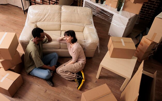 Divers mari et femme assis sur le sol de l'appartement et profitant de la relocalisation, pensant aux décorations du salon après avoir emménagé ensemble. Propriété familiale louée. Vue de dessus de.