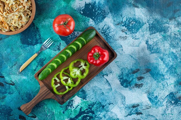 Diversement des légumes sur une planche à côté d'une fourchette et un bol de nouilles sur la table bleue.