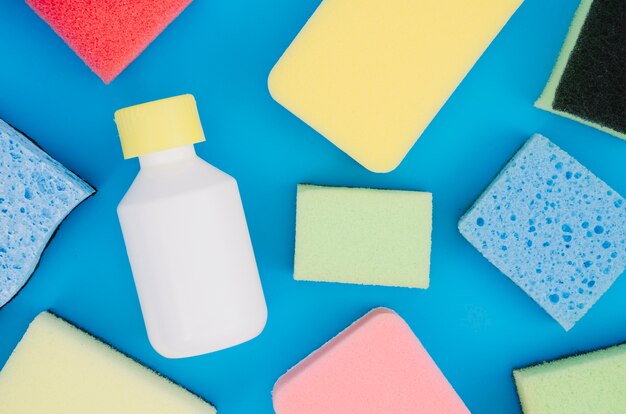 Diverses éponges colorées avec une bouteille sur fond bleu