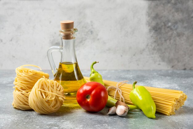 Diverses pâtes crues avec bouteille d'huile d'olive et de légumes sur table en marbre.