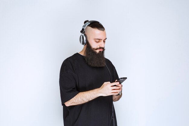 Dj avec barbe portant des écouteurs et mettant la musique de sa liste de lecture sur son smartphone.