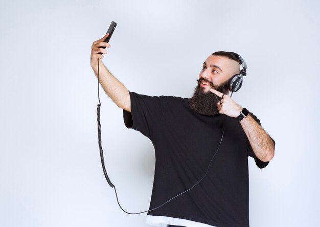 Dj avec barbe portant des écouteurs ouvrant l'appareil photo du smartphone et prenant son selfie.