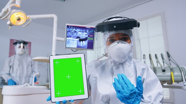 Docteur en costume ppe montrant une tablette avec écran vert, expliquant la radiographie dentaire et le diagnostic de l'infection des dents. Spécialiste de la stomatologie en combinaison pointant sur la maquette, l'espace de copie, l'affichage de la chrominance