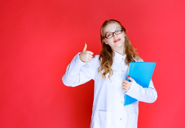 Docteur avec un dossier bleu montrant un signe de main réussi.