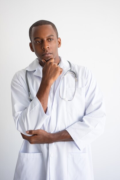 Docteur mâle noir songeur touchant le menton. Concept de décision médicale.