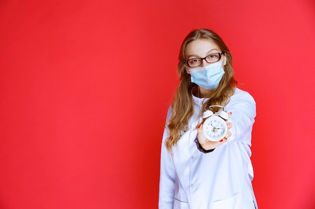 Docteur en masque facial montrant une horloge indiquant l'heure de prendre des médicaments.