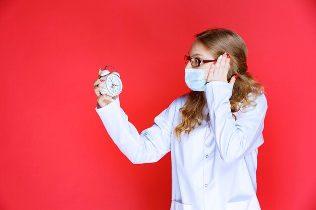 Docteur en masque facial tenant une horloge et semble confus.