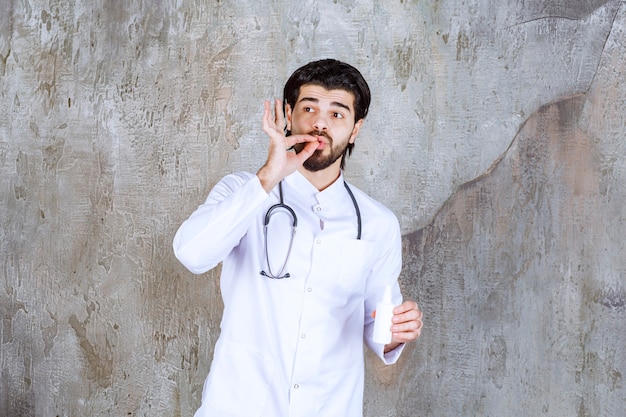 Docteur avec un stéthoscope tenant un tube blanc de spray désinfectant pour les mains et appréciant le produit.